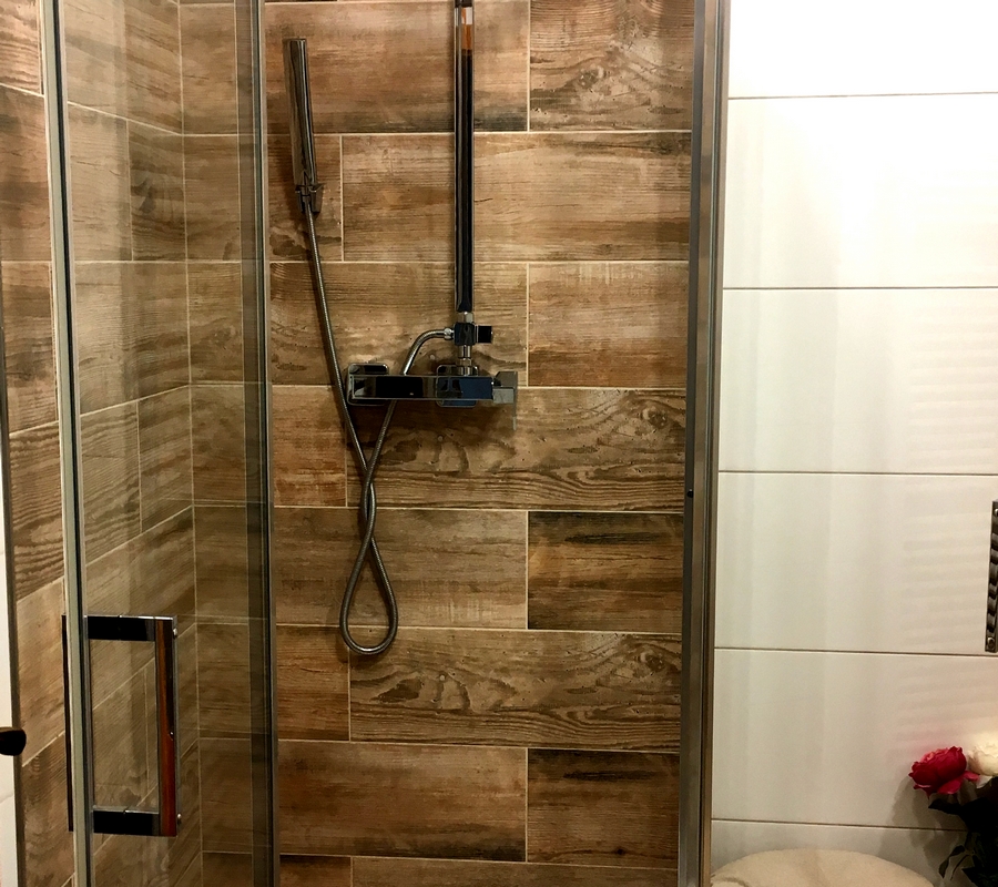 Detail sprchového koutu s dekorem dřeva, sprchová hadice.
