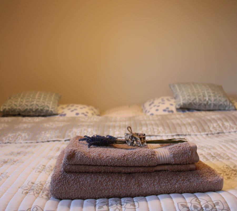 Pohled na béžové ručníky s květinou (levandule) na manželské posteli, zelenobílé povlečení
